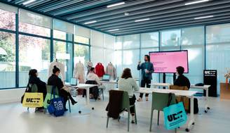 Un grupo de personas escucha a un instructor en un aula moderna con pantallas y escritorios.