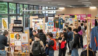 Una exposición con varios puestos de artistas y un público interesado en sus obras.