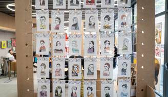 Una exposición de ilustraciones con retratos de diversas personas en tarjetas colgadas en un panel.