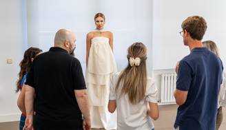 Un grupo de personas observa a una modelo que lleva un vestido blanco en un entorno interior.