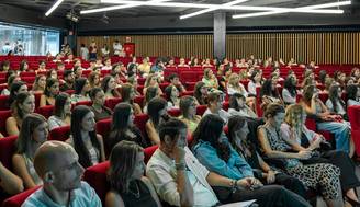 Una multitud de personas sentadas en un auditorio moderno con sillas rojas.