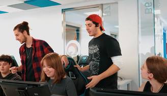 Un grupo de jóvenes se reúne en un ambiente de trabajo colaborativo, utilizando computadoras y compartiendo ideas.