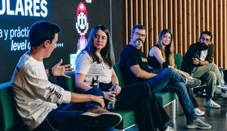 Un panel de discusión con cinco personas sentadas en un escenario, hablando sobre temas relacionados con los videojuegos.