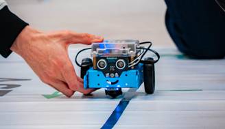 Un robot pequeño de color azul está siguiendo una línea en el suelo mientras una mano lo guía.