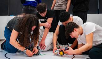 Un grupo de jóvenes trabaja en la construcción y programación de robots en un evento de robótica.