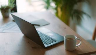 Una oficina acogedora con un portátil, una taza de café y plantas en el fondo.