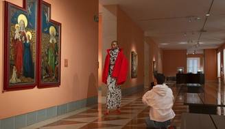 Una modelo posando en un museo frente a un par de pinturas religiosas mientras alguien le toma una foto.