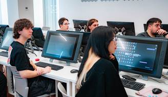 Un grupo de estudiantes sentados frente a computadoras en un aula moderna.