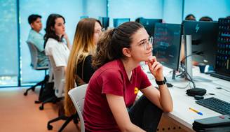 Un grupo de estudiantes en un aula de informática observa atentamente una presentación en sus computadoras.