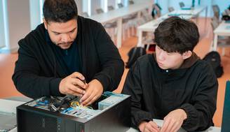 Dos personas están trabajando en un ordenador de mesa, una de ellas está manipulando el interior del equipo mientras la otra observa.