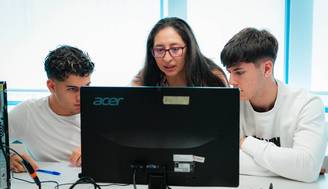 Tres personas observan atentamente una pantalla de ordenador en un entorno de aprendizaje.