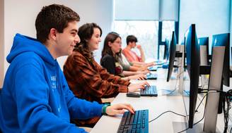 Un grupo de estudiantes sentado frente a computadoras en un aula.