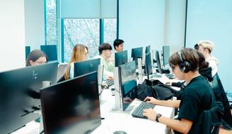 Un grupo de jóvenes sentados frente a computadoras en un aula moderna.