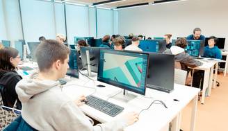 Un aula de computación con estudiantes trabajando en ordenadores mientras un profesor les dirige.