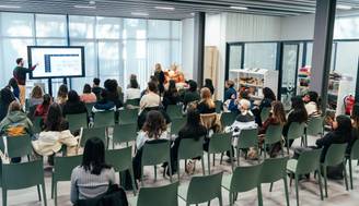 Una presentación en un aula con múltiples asistentes sentados en sillas, mirando hacia un expositor.