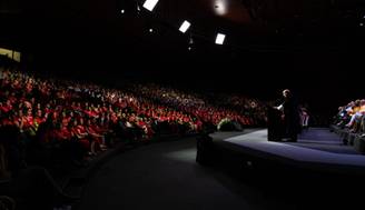 Un orador se dirige a una multitud numerosa en un evento en un auditorio.