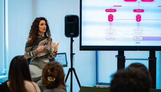 Una presentadora está explicando conceptos frente a una audiencia en una sala de conferencias.