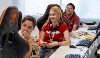 Un grupo de jóvenes sentados en un aula de computación, con sonrisas y auriculares puestos.