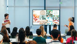 Una presentación en una clase con un expositor y una conferencista ante una pantalla con imágenes.