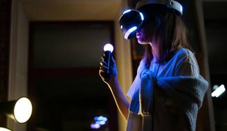 Una persona usando un visor de realidad virtual, sosteniendo un controlador iluminado en una habitación oscura.