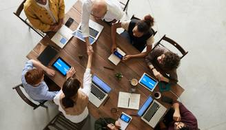 Un grupo de personas se reúne alrededor de una mesa de trabajo colaborando y utilizando tecnología.