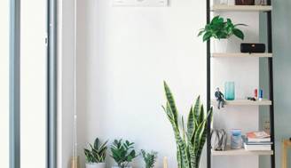 Una esquina moderna de una habitación con estantería, plantas y una obra de arte en la pared.