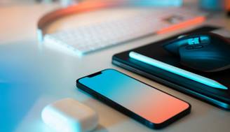 Una imagen que muestra un teléfono, auriculares, un ratón y una tablet sobre una mesa con iluminación tenue.