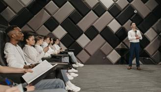 Un grupo de personas escuchando atentamente a un presentador en un ambiente de sala de conferencias.