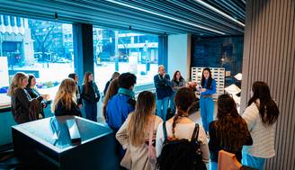 Un grupo de personas está escuchando a una mujer que habla en un ambiente moderno y acogedor.