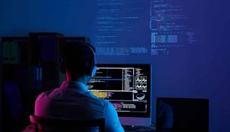 Un programador trabaja en su computadora mientras se proyectan códigos en la pared oscura.