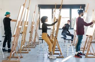 Un grupo de cuatro personas está pintando en un estudio con caballetes.