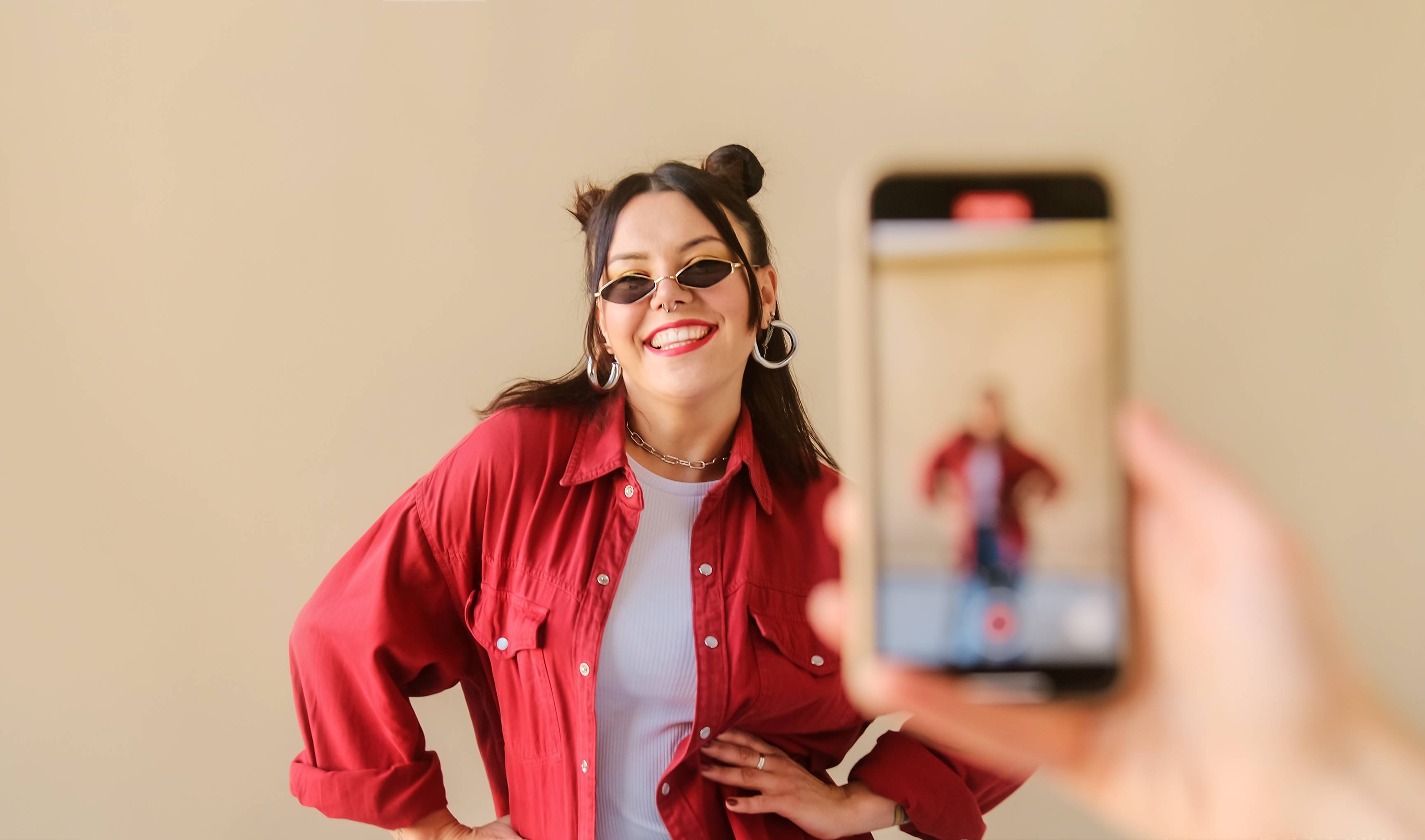 Una mujer sonriente posa para una fotografía mientras alguien la está grabando con un teléfono móvil.