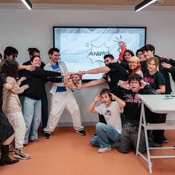 Un grupo de jóvenes se ríe y se divierte mientras posan en una sala de actividades con una pantalla de fondo que dice '¡Ánimo!'.