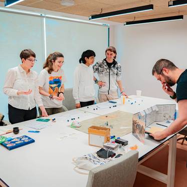 Un grupo de personas interactuando en una mesa de trabajo con diversos objetos y material de oficina.