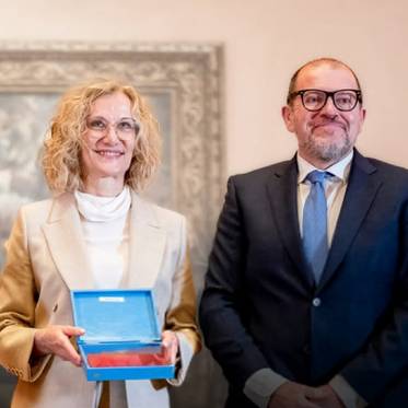Dos personas posan sonrientes, una de ellas sostiene una caja en un ambiente elegante.