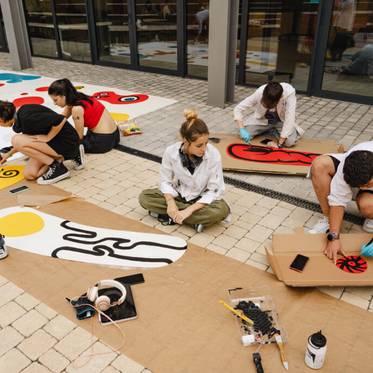 Un grupo de personas está pintando en una superficie al aire libre con colores vivos y diseños variados.