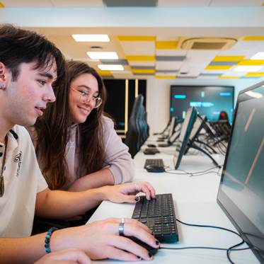 Dos jóvenes trabajan juntos en una computadora en un aula moderna.
