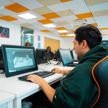 Un joven trabaja en una computadora en un aula moderna con decoración colorida.