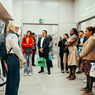 Un grupo de personas escucha atentamente a una expositora en un espacio de fabricación creativa.