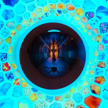 La imagen muestra un pasillo iluminado con luces azules y un diseño de hexágonos coloridos en el techo.