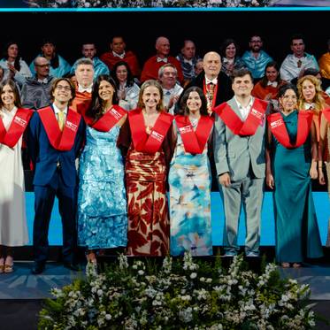Un grupo de graduados sonríe en una ceremonia de graduación, vistiendo togas y bufandas rojas.