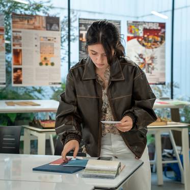 Una joven revisa documentos y materiales en una mesa de trabajo en un entorno creativo.