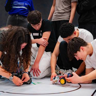 Un grupo de jóvenes trabaja en la construcción y programación de robots en un evento de robótica.