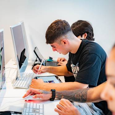 Un grupo de jóvenes trabaja en computadoras en un aula moderna.