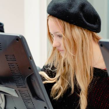 Una joven con sombrero se concentra en la pantalla de una computadora.