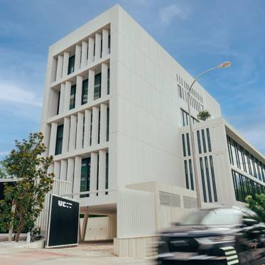 Edificio moderno con fachada blanca y vegetación alrededor.