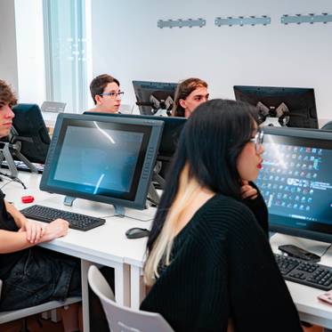 Un grupo de estudiantes sentados frente a computadoras en un aula moderna.