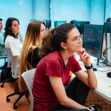 Un grupo de estudiantes en un aula de informática observa atentamente una presentación en sus computadoras.