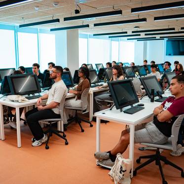 Un grupo de estudiantes sentados en un aula con computadoras.