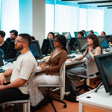 Un grupo de personas sentadas en un aula frente a computadoras en un entorno moderno.
